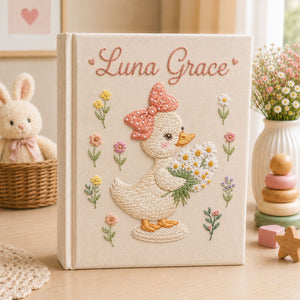 Personalized hand embroidered photo album featuring a cute duckling with a polka dot bow holding a daisy bouquet surrounded by pastel flowers and custom name embroidery