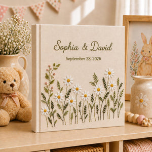 Personalized embroidered wedding photo album with white daisy flowers, botanical greenery embroidery, custom couple names, wedding date, and elegant linen hardcover design