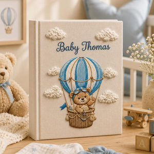 Personalized embroidered baby photo album featuring pilot teddy bear in blue hot air balloon with fluffy clouds