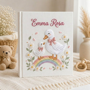 Personalized hand embroidered photo album featuring a swan mother and baby standing on a pastel rainbow surrounded by daisies and floral details