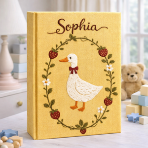 Personalized hand embroidered photo album featuring a white goose surrounded by a floral wreath on a yellow linen cover