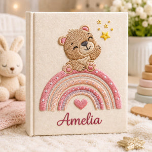 Personalized hand embroidered baby photo album featuring teddy bear sitting on pastel rainbow with stars and heart accents