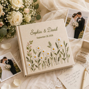 Personalized embroidered wedding photo album with white daisy flowers, botanical greenery embroidery, custom couple names, wedding date, and elegant linen hardcover design