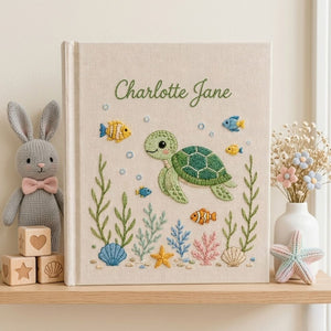Personalized hand embroidered photo album featuring a cute sea turtle swimming with tropical fish, coral, seashells, and ocean plants on a premium linen cover customized with a baby name