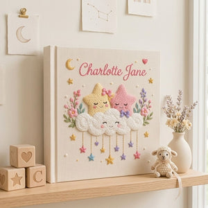 Personalized hand embroidered photo album featuring smiling stars resting on fluffy clouds with hanging pastel stars and floral accents on a premium linen cover customized with a baby name