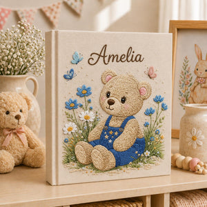 Personalized hand embroidered baby photo album with teddy bear in blue overalls surrounded by flowers and butterflies