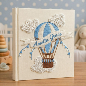 Personalized hand embroidered photo album featuring a vintage hot air balloon floating among clouds and stars on a linen cover