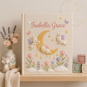 Personalized hand embroidered photo album featuring fairy bunnies around a golden crescent moon with stars, flowers, butterflies, and clouds on a premium linen cover customized with a baby name