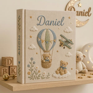 Personalized hand embroidered photo album featuring a teddy bear in a vintage hot air balloon with a classic biplane, clouds, stars, wildflowers, custom name and year embroidery on a premium linen cover