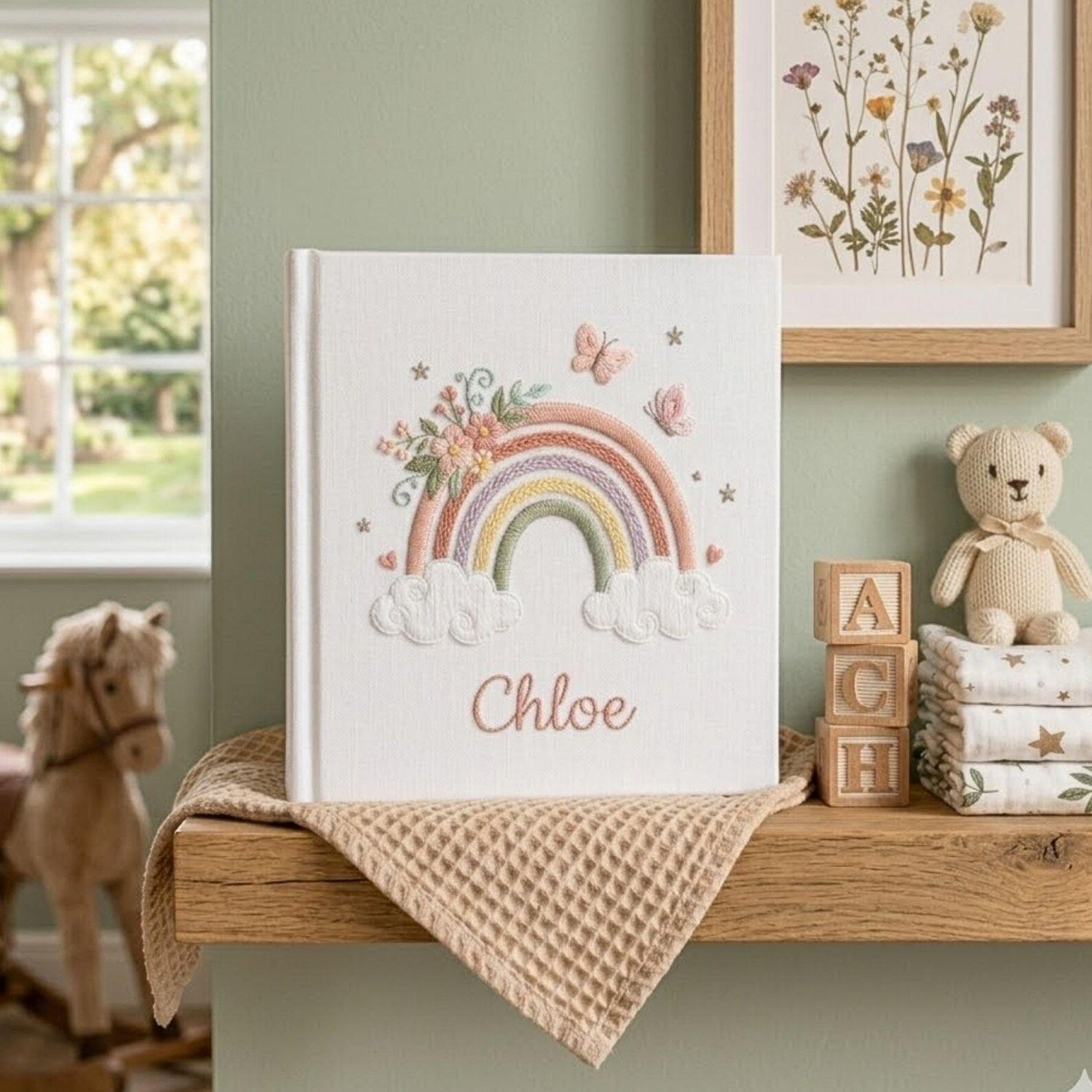 Custom embroidered baby photo album with pastel rainbow, butterflies, floral embroidery, fluffy clouds, and personalized name