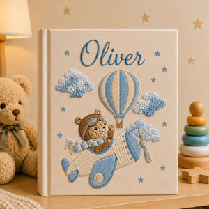 Personalized hand embroidered photo album featuring a teddy bear pilot flying a vintage airplane with hot air balloons, clouds and stars