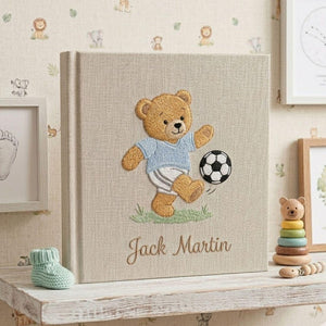 Personalized hand embroidered photo album featuring a teddy bear playing soccer with a football and custom baby name on linen cover
