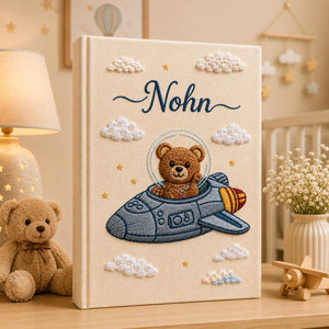 Personalized embroidered baby photo album featuring teddy bear astronaut riding a space rocket with fluffy clouds