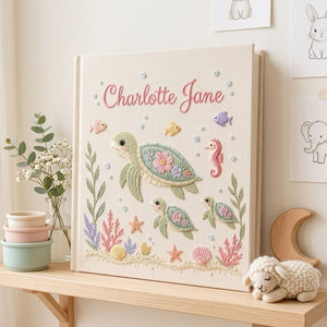 Personalized hand embroidered photo album featuring a sea turtle family with coral reefs, tropical fish, seashells, starfish, and seahorse on a premium linen cover customized with a baby name