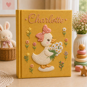Personalized hand embroidered photo album featuring a cute duckling with a polka dot bow holding a daisy bouquet surrounded by pastel flowers and custom name embroidery