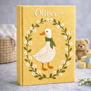 Personalized hand embroidered photo album featuring a white goose surrounded by a floral wreath on a yellow linen cover