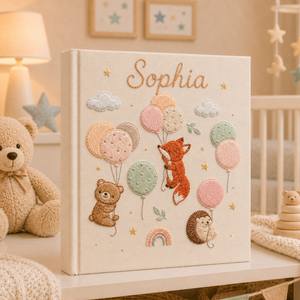 Personalized hand embroidered photo album featuring woodland animals with pastel balloons, clouds, stars, and rainbow details on a linen cover