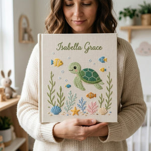 Personalized hand embroidered photo album featuring a cute sea turtle swimming with tropical fish, coral, seashells, and ocean plants on a premium linen cover customized with a baby name