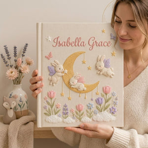 Personalized hand embroidered photo album featuring fairy bunnies around a golden crescent moon with stars, flowers, butterflies, and clouds on a premium linen cover customized with a baby name