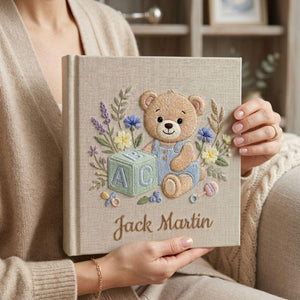 Personalized hand embroidered photo album featuring teddy bear in blue overalls with alphabet block and floral details on linen cover