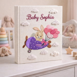 Personalized hand embroidered photo album featuring a bunny flying a purple airplane with heart-shaped balloons and fluffy clouds