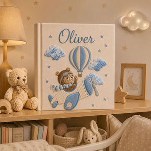 Personalized hand embroidered photo album featuring a teddy bear pilot flying a vintage airplane with hot air balloons, clouds and stars