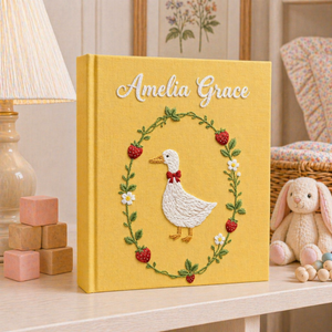 Personalized hand embroidered photo album featuring a white goose surrounded by a floral wreath on a yellow linen cover