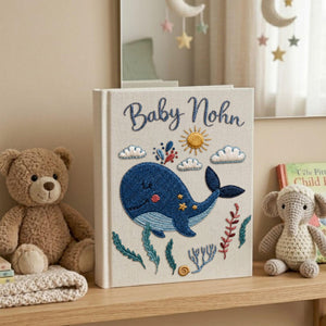 Personalized embroidered baby photo album with smiling whale, ocean plants, clouds, sunshine, and custom name embroidery