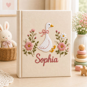 Personalized hand embroidered photo album featuring a white goose with pink bow surrounded by delicate pink flowers and custom name embroidery on linen cover