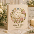 Personalized embroidered wedding photo album with floral swan embroidery, pastel botanical flowers, custom names, wedding date, and linen hardcover design