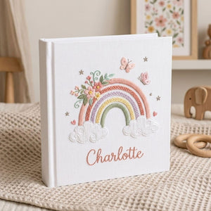 Custom embroidered baby photo album with pastel rainbow, butterflies, floral embroidery, fluffy clouds, and personalized name