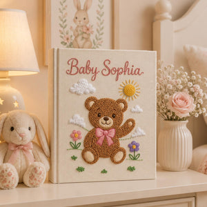 Personalized embroidered baby photo album with teddy bear, sunshine, clouds, and pastel flowers nursery design