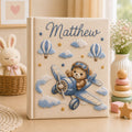 Personalized hand embroidered photo album featuring a teddy bear pilot flying a vintage airplane with clouds hot air balloons and stars on a linen cover