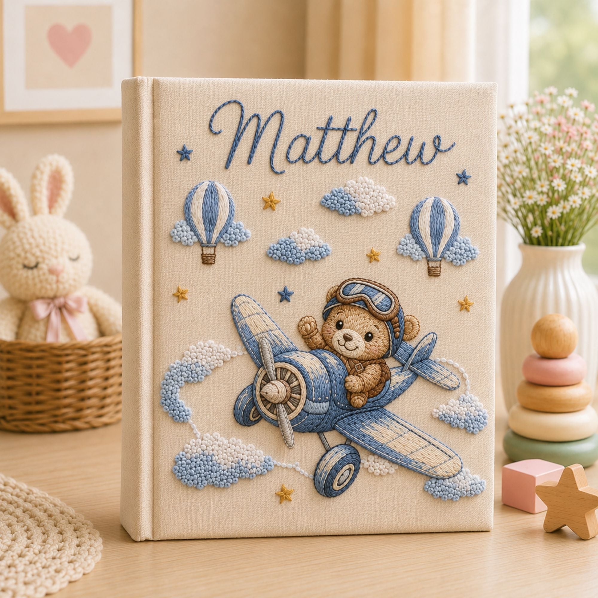 Personalized hand embroidered photo album featuring a teddy bear pilot flying a vintage airplane with clouds hot air balloons and stars on a linen cover