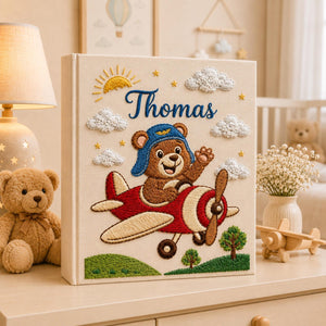 Personalized hand embroidered baby photo album with teddy bear pilot flying a vintage airplane surrounded by clouds and sunshine