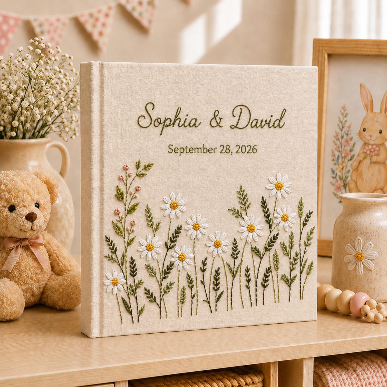 Personalized embroidered wedding photo album with white daisy flowers, botanical greenery embroidery, custom couple names, wedding date, and elegant linen hardcover design