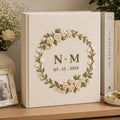 Neutral floral embroidered wedding albums with ivory roses, botanical wreaths, geometric floral frames, and personalized couple names on linen covers