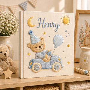 Personalized hand embroidered baby photo album featuring teddy bear driving a pastel blue vintage car with balloon, moon, stars, and sunshine accents