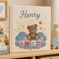 Personalized hand embroidered photo album featuring a teddy bear with a pacifier sitting on clouds beneath a crescent moon with colorful ABC blocks and stars