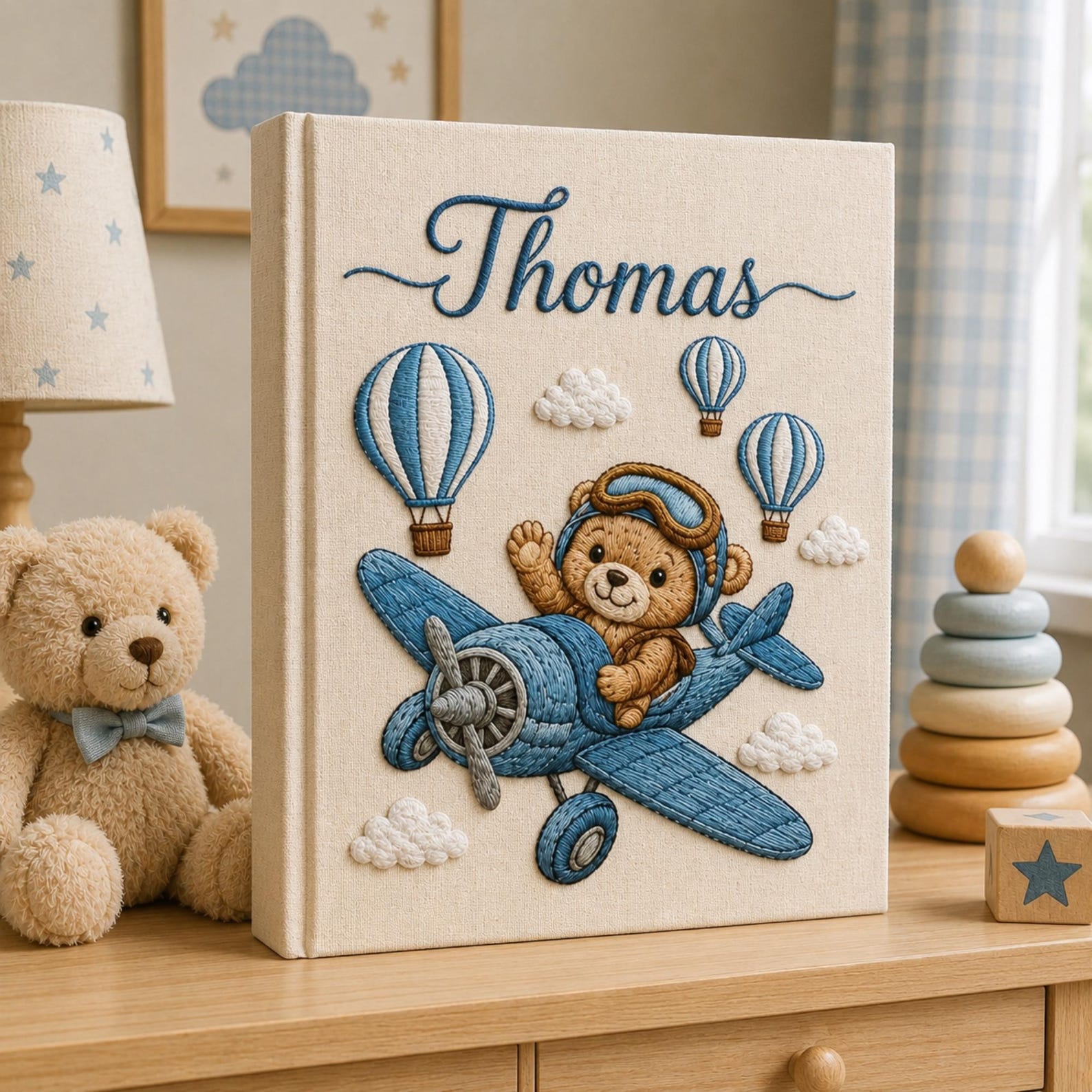 Personalized embroidered baby photo album featuring teddy bear pilot flying a vintage blue airplane with hot air balloons and clouds