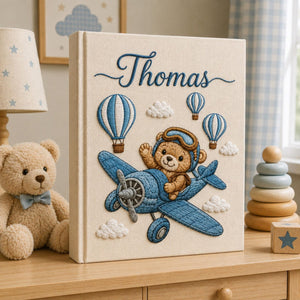Personalized embroidered baby photo album featuring teddy bear pilot flying a vintage blue airplane with hot air balloons and clouds