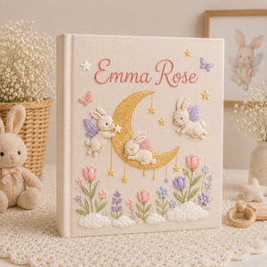Personalized hand embroidered photo album featuring fairy bunnies around a golden crescent moon with stars, flowers, butterflies, and clouds on a premium linen cover customized with a baby name