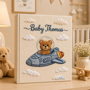 Personalized embroidered baby photo album featuring teddy bear astronaut riding a space rocket with fluffy clouds