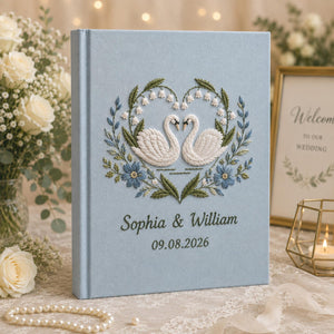 Personalized embroidered wedding photo album with white swans, blue floral heart wreath embroidery, custom couple names, wedding date, and elegant blue linen hardcover design