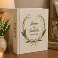 Personalized embroidered wedding photo album with lily of the valley floral wreath embroidery, custom couple names, wedding date, and elegant linen hardcover design