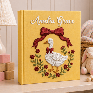 Personalized hand embroidered photo album featuring an elegant goose surrounded by a floral berry wreath on a golden linen cover