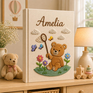 Personalized embroidered baby photo album featuring teddy bear holding butterfly net surrounded by flowers and butterflies