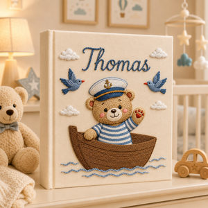 Personalized hand embroidered photo album featuring a little sailor character in a wooden boat with bluebirds and clouds on a linen cover