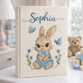 Personalized hand embroidered photo album featuring a cute bunny wearing blue overalls and a bow tie surrounded by blue butterflies and flowers on a linen cover