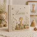 Personalized hand embroidered photo album featuring a baby giraffe riding a vintage train surrounded by daisies, butterflies, and honeybees on a premium linen cover customized with a baby name